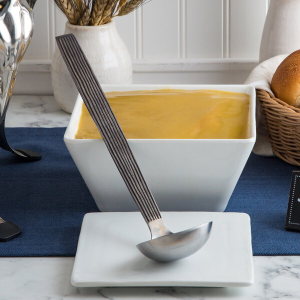A close up of a silver American Metalcraft wavy ladle in a bowl of yellow liquid.