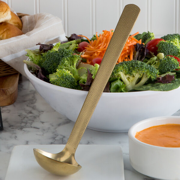 A bowl of salad with a ladle of American Metalcraft GVHML Hammered Gold Vintage Ladle.