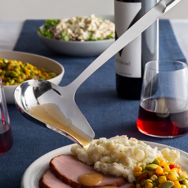 A plate of food with an American Metalcraft stainless steel spout ladle being poured over it.