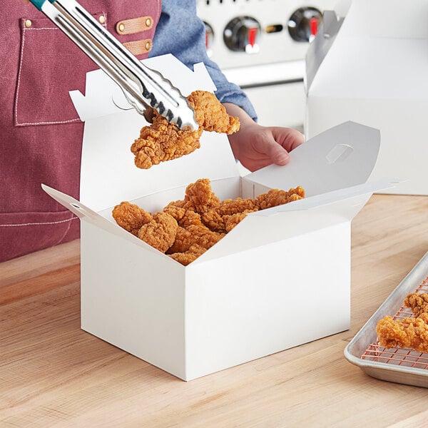 A person holding a White Barn take out lunch box with fried chicken inside.