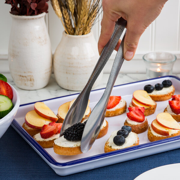 A person using American Metalcraft vintage stainless steel tongs to pick up apple slices from a plate.