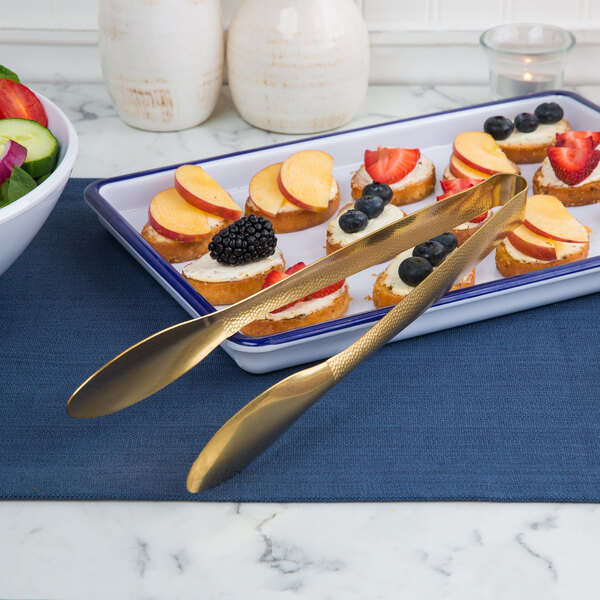 Gold tongs holding a plate of fruit and cheese with bread