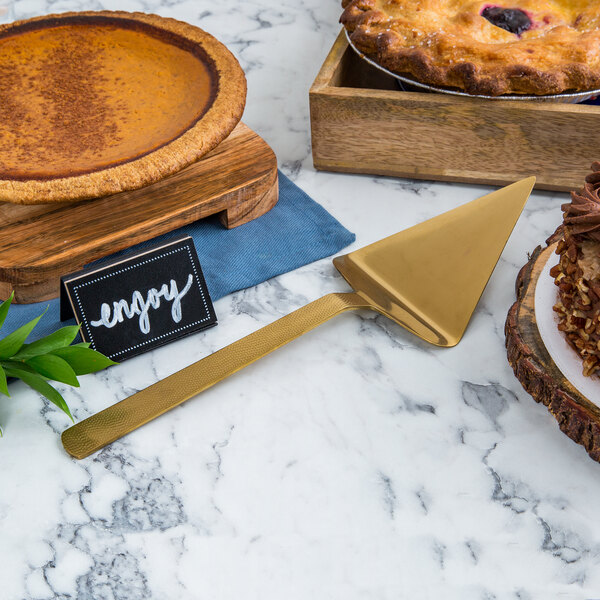 A pie and a gold hammered pie server on a marble table.