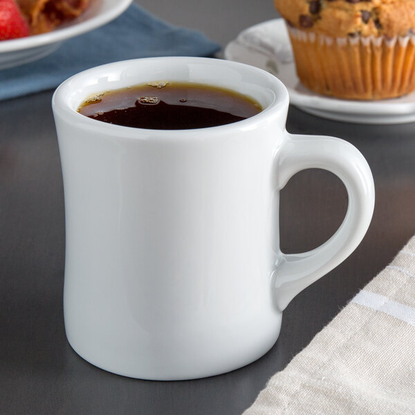 A Tuxton white porcelain diner mug filled with coffee on a table with a muffin.