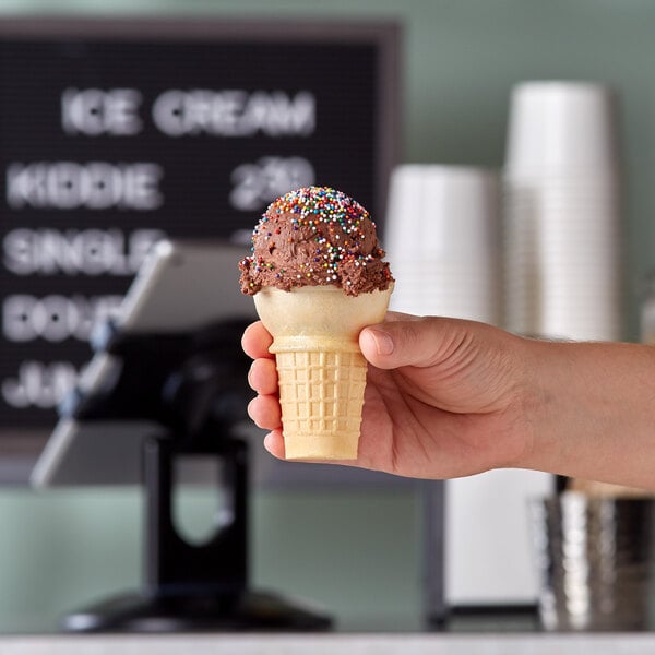 A hand holding a JOY flat bottom cake cone full of ice cream.