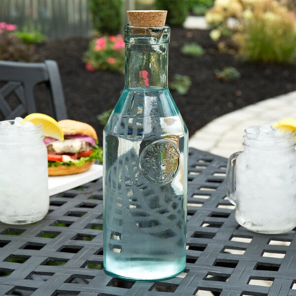 A Tablecraft green glass bottle with cork on a table with a glass of water.