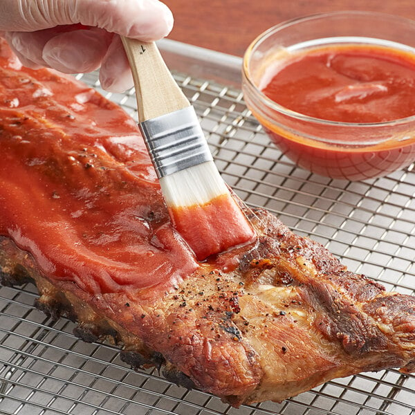 A person using a paint brush to apply Cattlemen's BBQ sauce to a piece of meat.