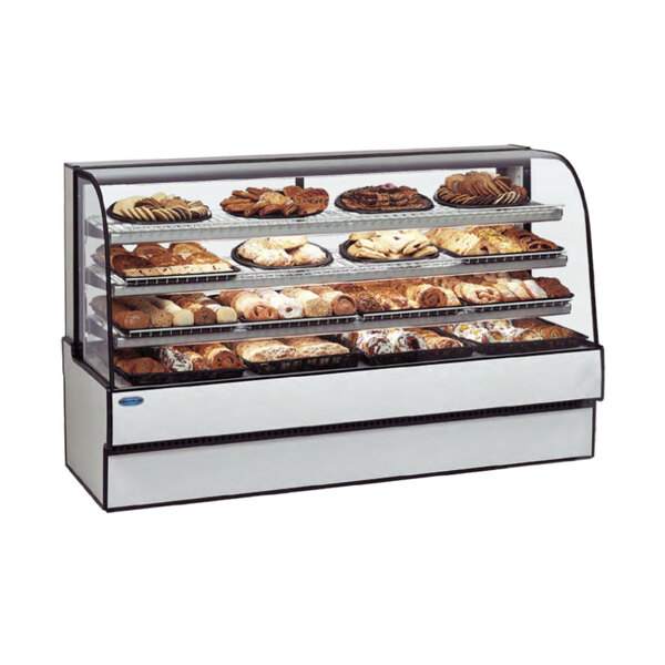 A Federal Industries curved glass refrigerated bakery case on a counter filled with different types of pastries.