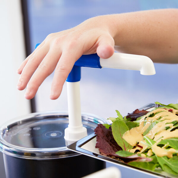 A hand using a white and blue Cambro cold pump to serve salad into a container.