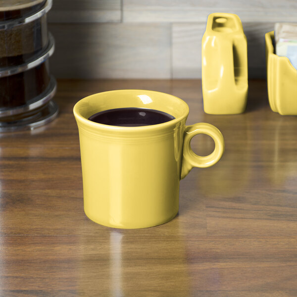 A yellow Fiesta china mug with a handle on a wooden surface.