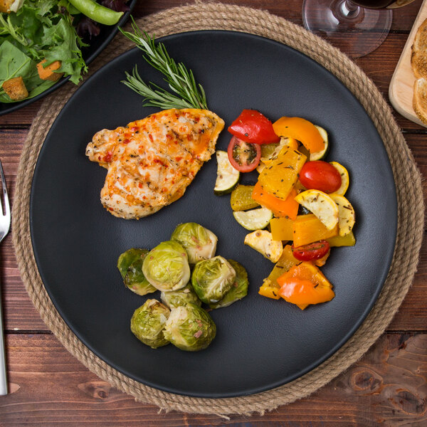 A TuxTrendz Zion matte black china plate with chicken, vegetables, and a fork.