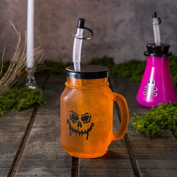 A glass jar with a Jack-O'-Lantern face drawn on it with a straw in it.