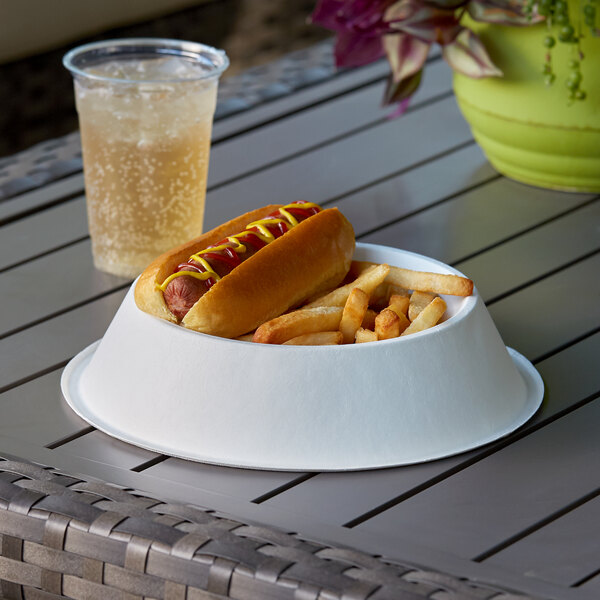 A hot dog and french fries in a Doggie Bagasse bowl on a table with a drink.