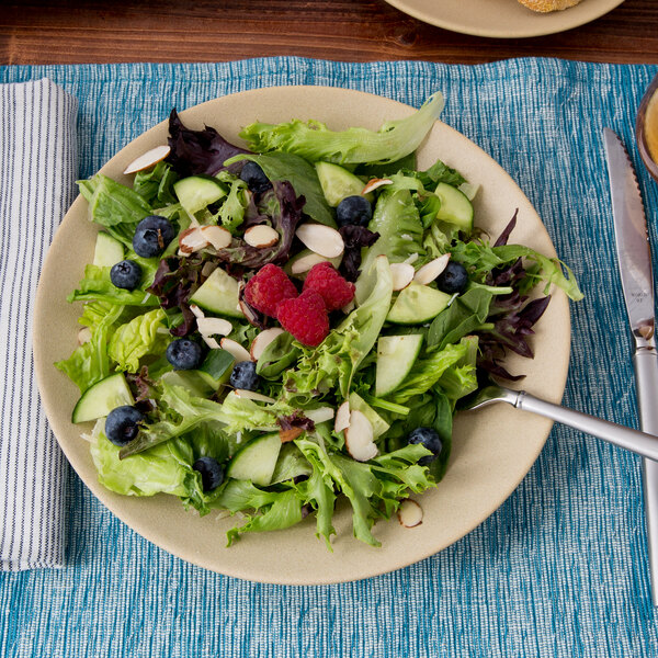 A Tuxton TuxTrendz matte beige china plate with a salad of berries and nuts.