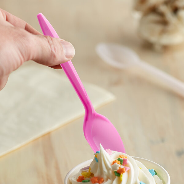 A hand holding a pink spoon over a cup of ice cream.