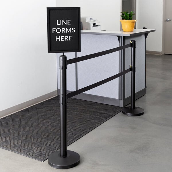 A Lancaster Table & Seating ADA compliant stanchion with a black frame and a white sign that says "Line Forms Here" with clear covers.