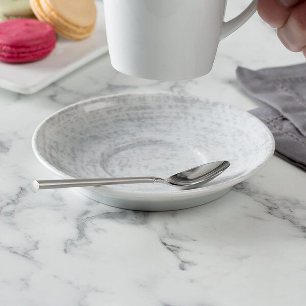 A hand holding a Schonwald Shabby Chic grey round porcelain saucer under a white cup.