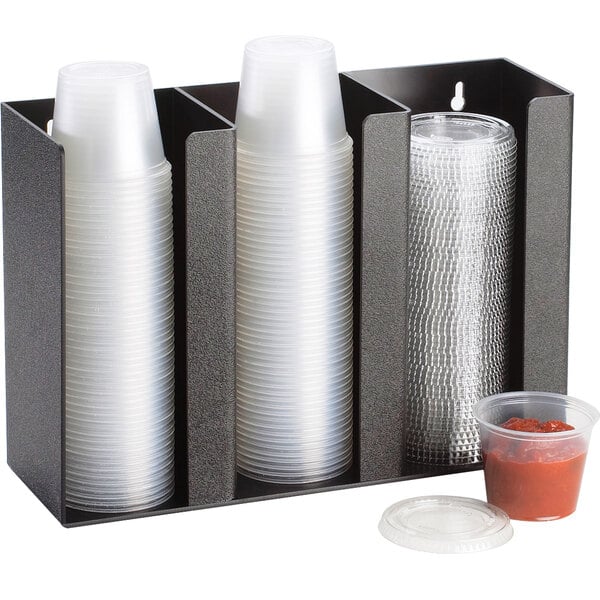 A black Cal-Mil countertop organizer with 3 sections holding plastic cups and a container.