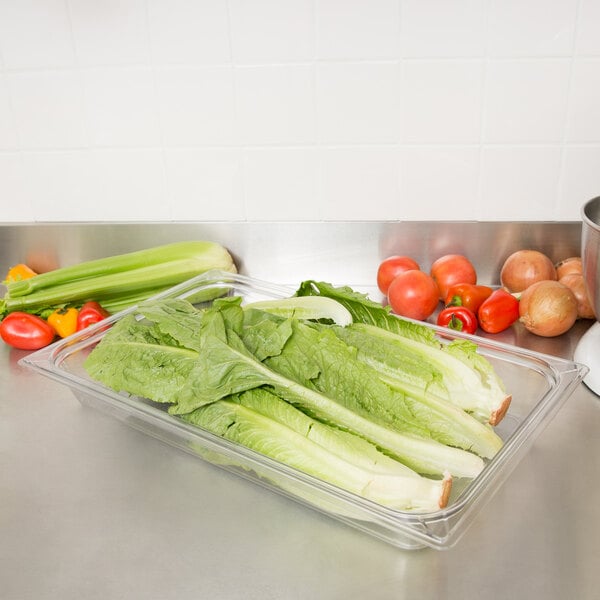 A Carlisle clear plastic food pan filled with lettuce and tomatoes on a counter.