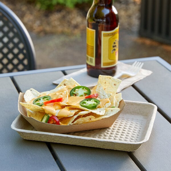 A rectangular paper tray of nachos with cheese and jalapenos with a bottle of beer on a table.