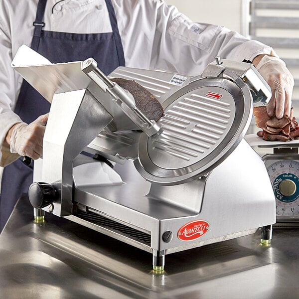 A person using an Avantco manual meat slicer to cut meat on a cutting board.