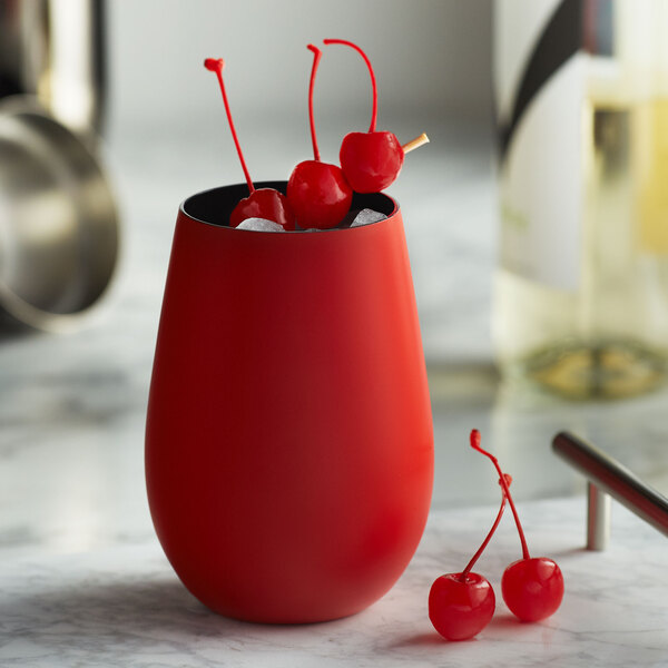 A close-up of a matte red Stolzle stemless wine glass with cherries in it.