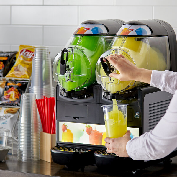 A woman pouring yellow juice into a Vollrath dual frozen beverage machine.