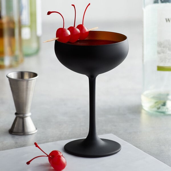 A black Stolzle coupe glass with a drink and cherries on it.