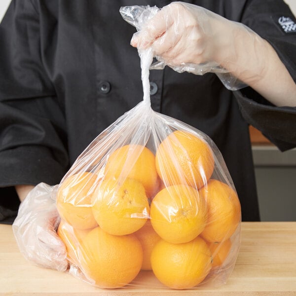A person in a black coat holding a plastic bag of oranges.