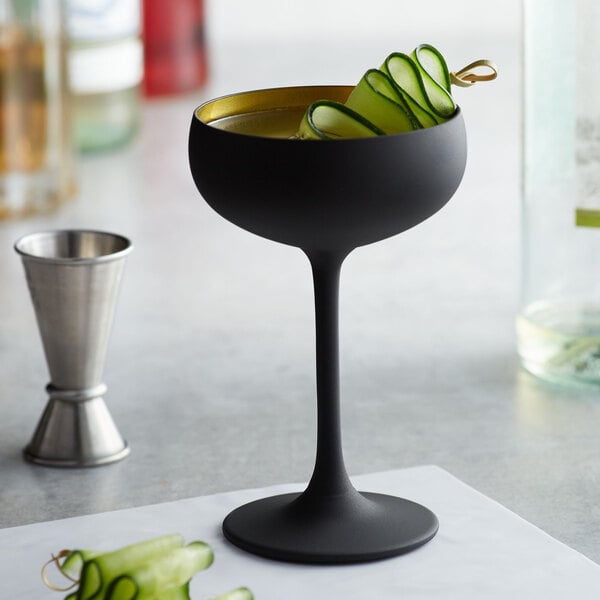 A black Stolzle coupe glass with cucumber slices in it.