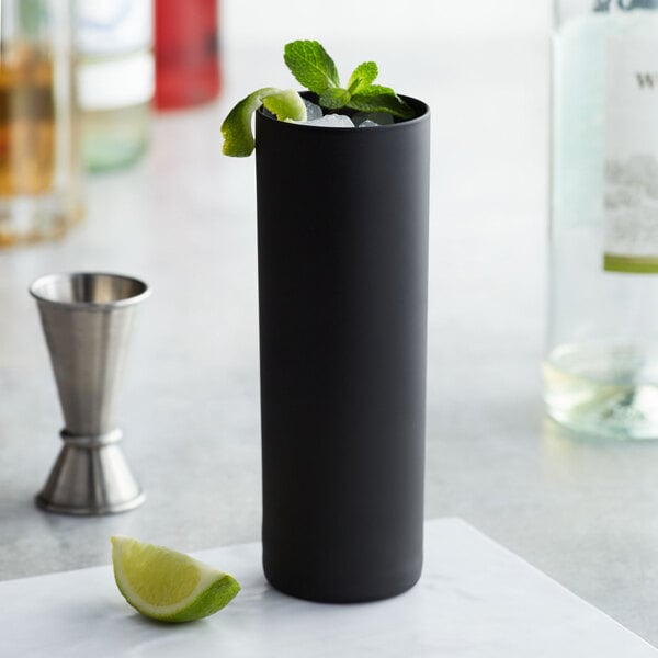 A black Stolzle longdrink / collins glass with ice and mint leaves on top and a slice of lime.