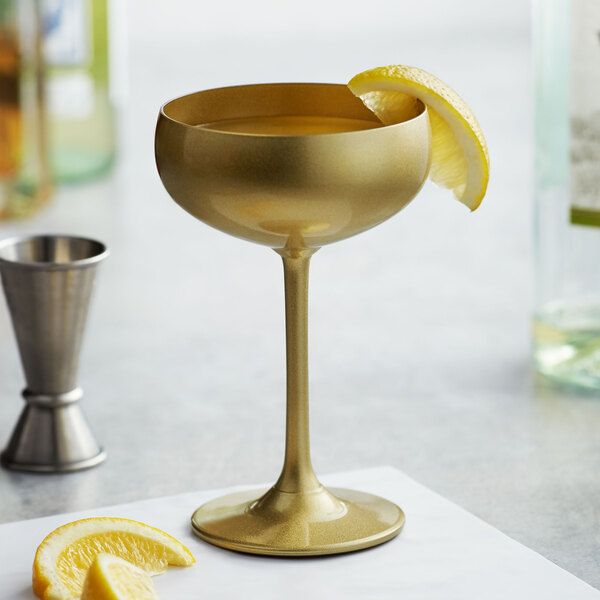A close-up of a Stolzle gold coupe glass with liquid and a lemon wedge