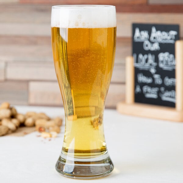 A Libbey giant pilsner glass filled with beer on a table.