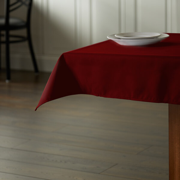 A square burgundy Intedge tablecloth on a table with a plate.