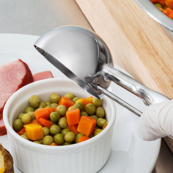 A gloved hand using a Vollrath #12 stainless steel squeeze handle disher to scoop food into a bowl.