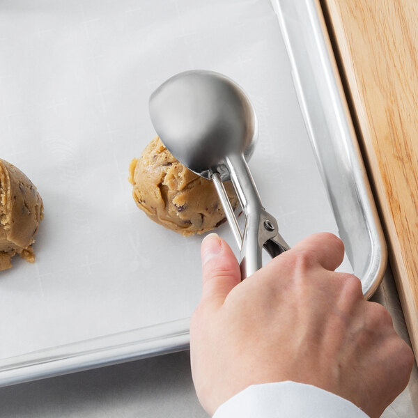 A hand using a Vollrath #16 stainless steel ice cream scoop to scoop cookie dough.
