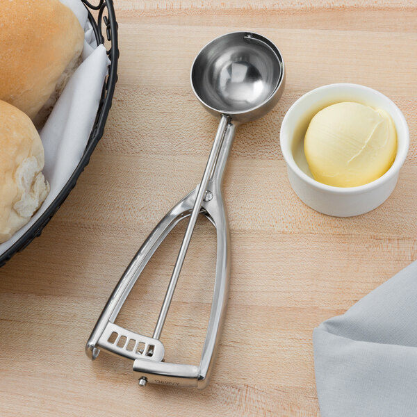 A Vollrath stainless steel ice cream scoop with a bowl of butter next to a bowl of bread.