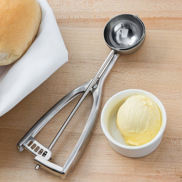 A Vollrath stainless steel disher filled with butter next to a bowl of bread.