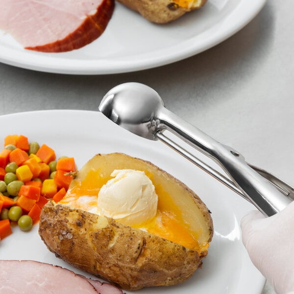 A baked potato with a scoop of butter on top served on a plate with a Vollrath stainless steel disher.