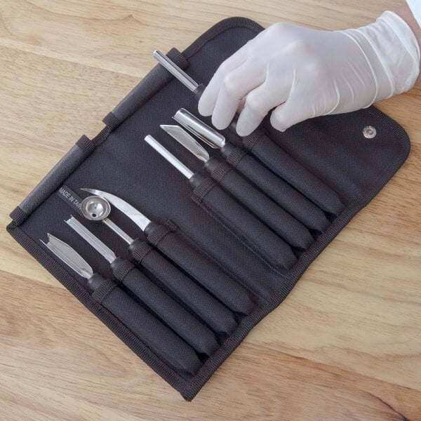 A hand in a white glove holding a Mercer Culinary garnish kit in a black case.