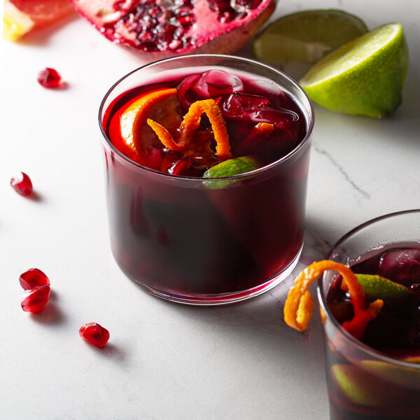 A Spanish style rocks glass filled with red liquid with lime and orange slices.
