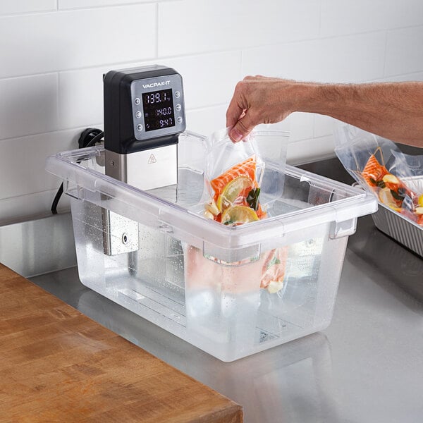 A person using a VacPak-It SV08 sous vide circulator to cook food in a plastic container.