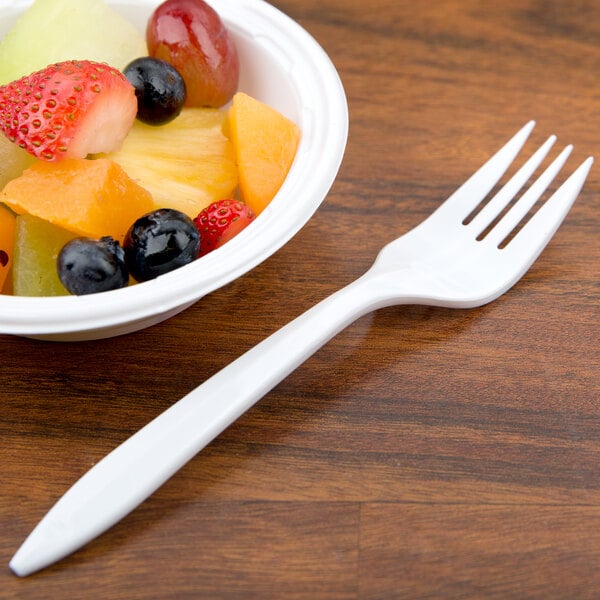 A bowl of fruit with a Dart white plastic fork on a table.