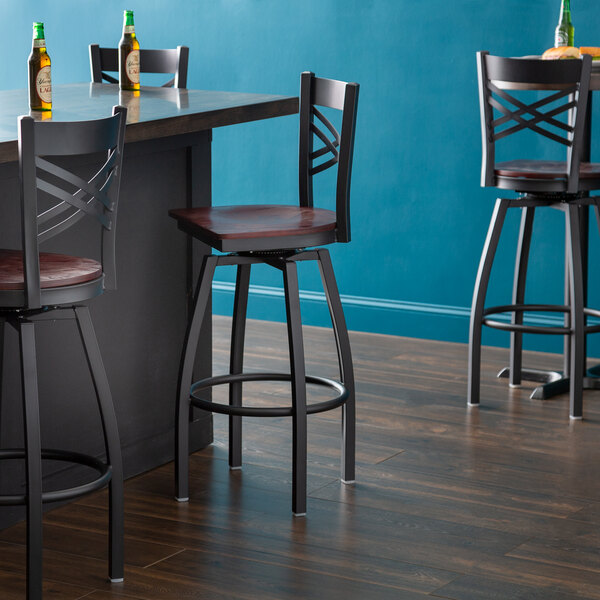 A Lancaster Table & Seating black swivel bar stool with a mahogany wood seat and back.