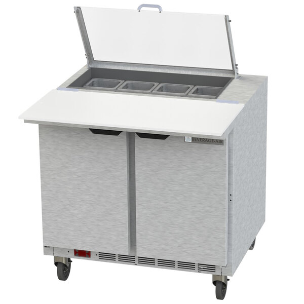 A Beverage-Air stainless steel sandwich prep table with clear lids open over food.