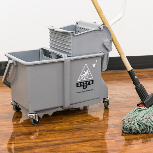 A Unger grey mop bucket on a wood floor.