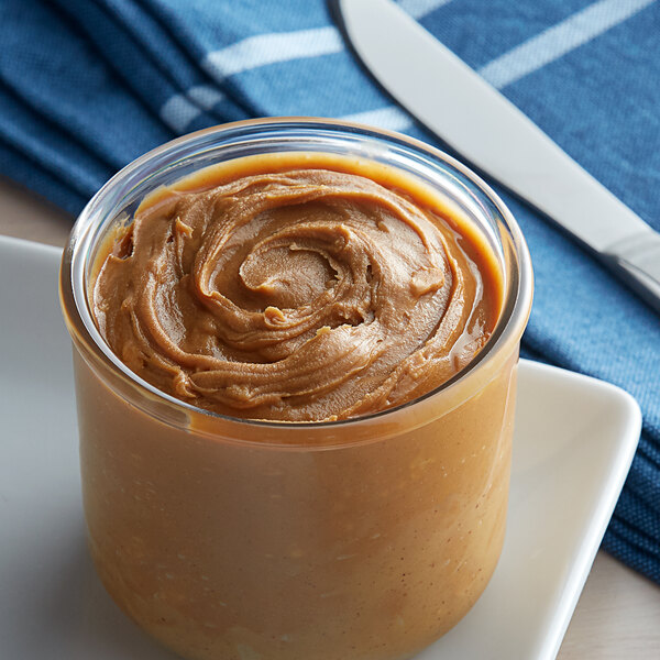 A jar of Bulk Crunchy Peanut Butter on a plate next to a knife.