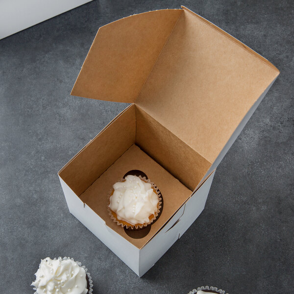 A cupcake with white frosting in a Baker's Mark white cupcake box.