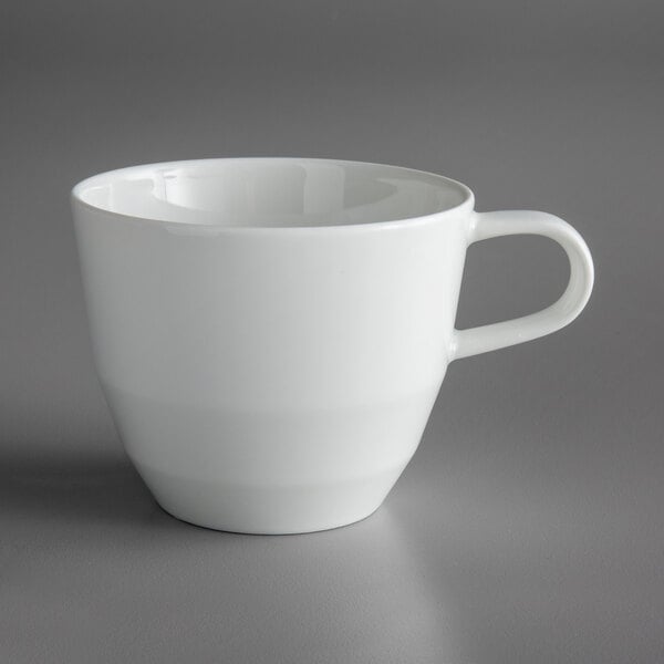 A Schonwald bone white porcelain tall cup with a handle on a gray surface.