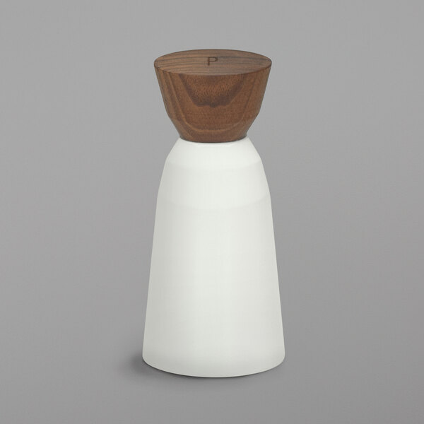 A Schonwald bone white porcelain pepper mill with a wooden top.